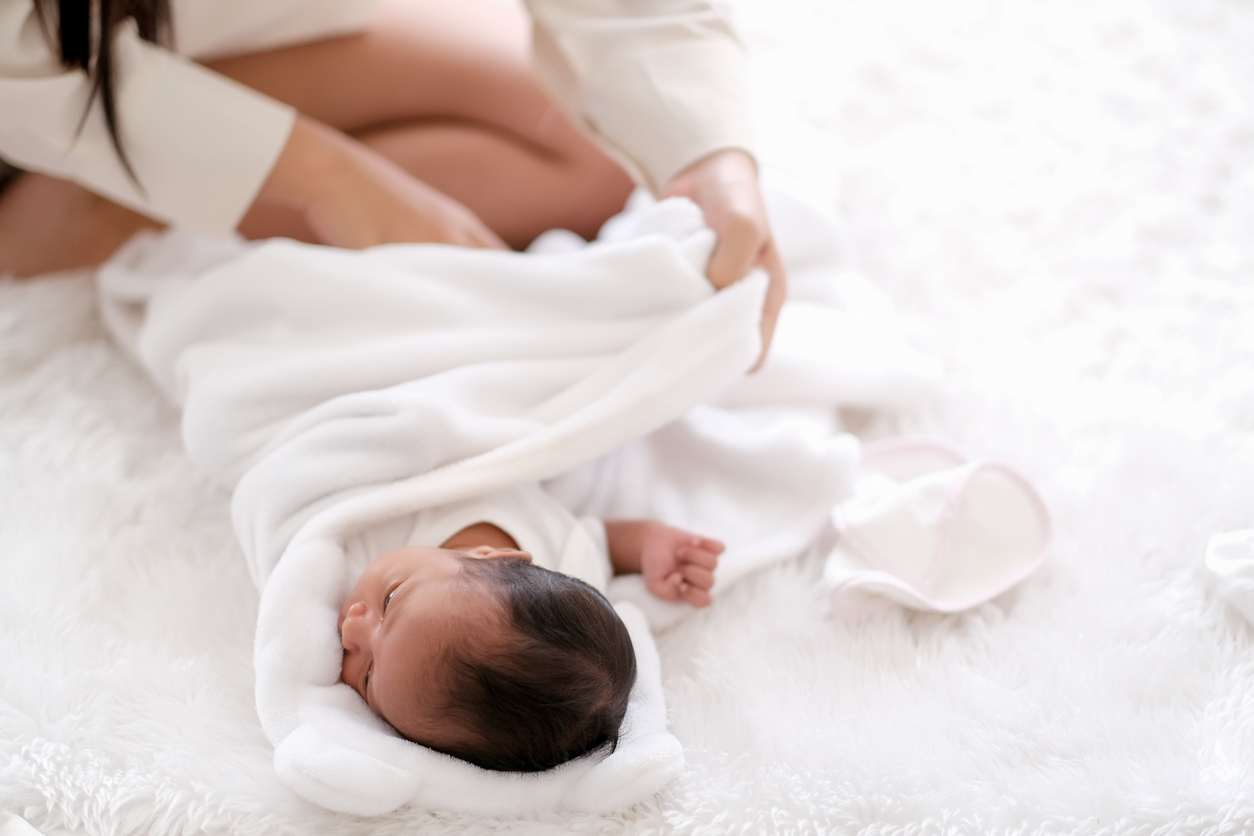 Parent swaddling a newborn baby using a soft cotton blanket.